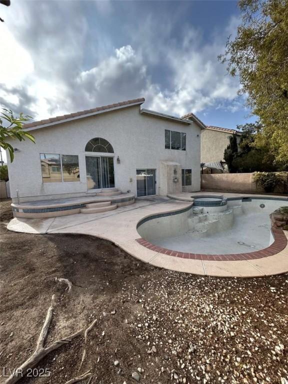 rear view of property featuring a tile roof, stucco siding, a patio, and a fenced in pool
