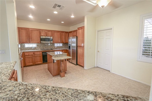 kitchen featuring light stone counters, tasteful backsplash, brown cabinetry, visible vents, and black appliances