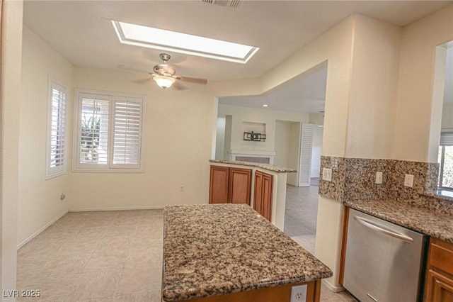 kitchen featuring light stone counters, a skylight, brown cabinets, and stainless steel dishwasher