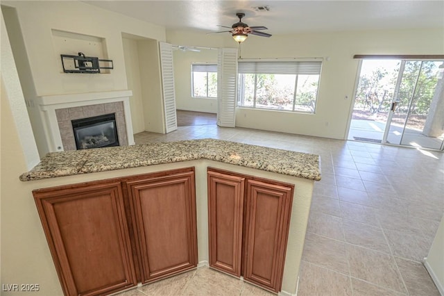 kitchen featuring a ceiling fan, a fireplace, light stone countertops, open floor plan, and visible vents