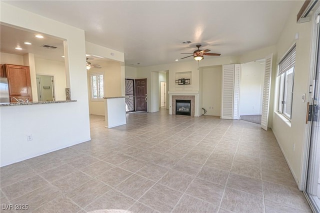 unfurnished living room featuring visible vents, a glass covered fireplace, and a ceiling fan