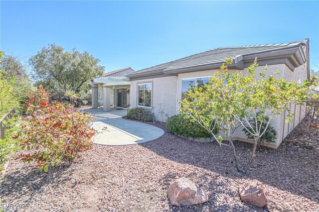 back of house featuring stucco siding, a tiled roof, a pergola, and a patio area