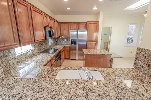 kitchen featuring light stone countertops, brown cabinetry, black appliances, and decorative backsplash