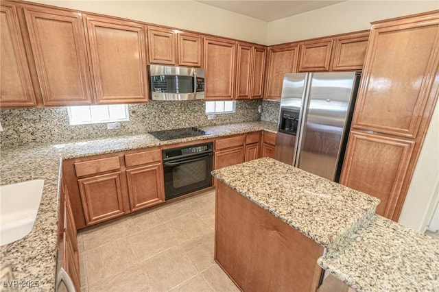 kitchen with backsplash, light stone countertops, black appliances, and brown cabinets