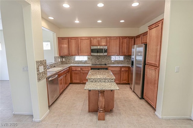 kitchen with decorative backsplash, appliances with stainless steel finishes, a sink, light stone counters, and a center island