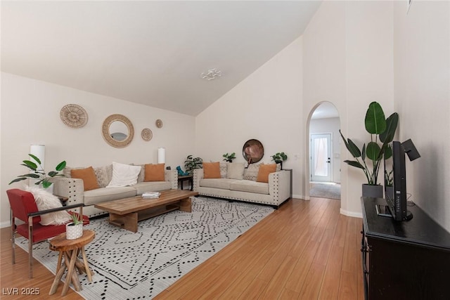 living area featuring arched walkways, light wood-type flooring, high vaulted ceiling, and baseboards