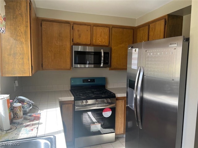 2541 Love St, Las Vegas, NV 89121 - kitchen featuring appliances with stainless steel finishes, tile counters, light tile patterned floors, and brown cabinetry