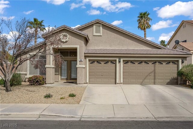 view of front of home with driveway, a garage, a tile roof, stucco siding, and french doors