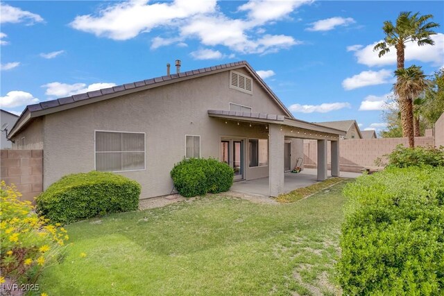 rear view of house with fence, stucco siding, a yard, and a patio