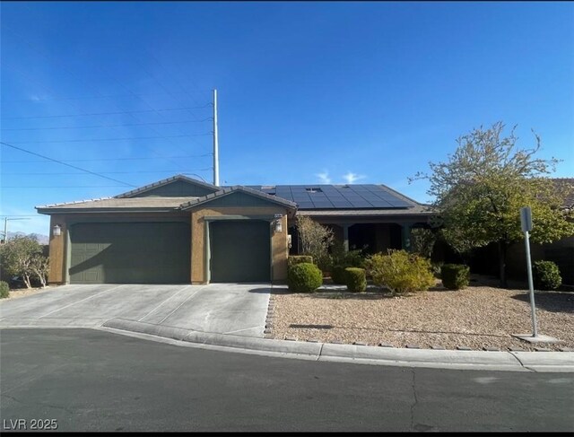 ranch-style house featuring a garage, roof mounted solar panels, and concrete driveway