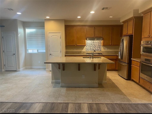 kitchen with under cabinet range hood, stainless steel appliances, brown cabinets, and visible vents