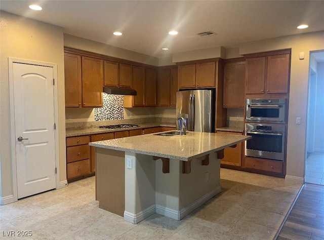 kitchen with visible vents, light stone countertops, under cabinet range hood, a sink, and appliances with stainless steel finishes