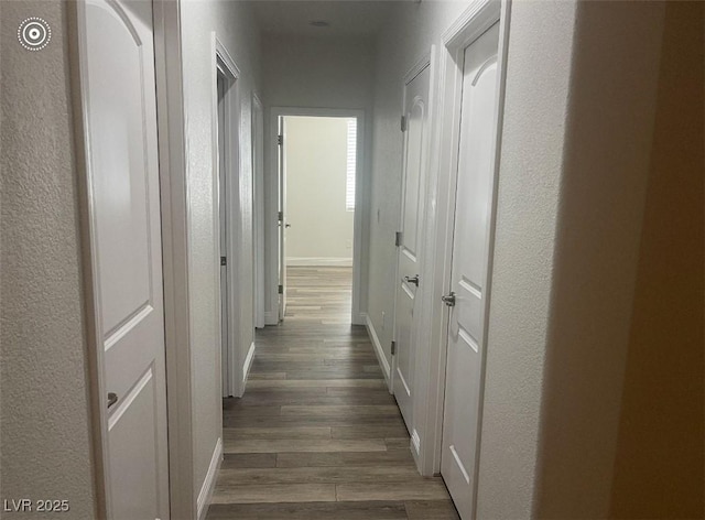 hall with a textured wall, baseboards, and dark wood-style floors