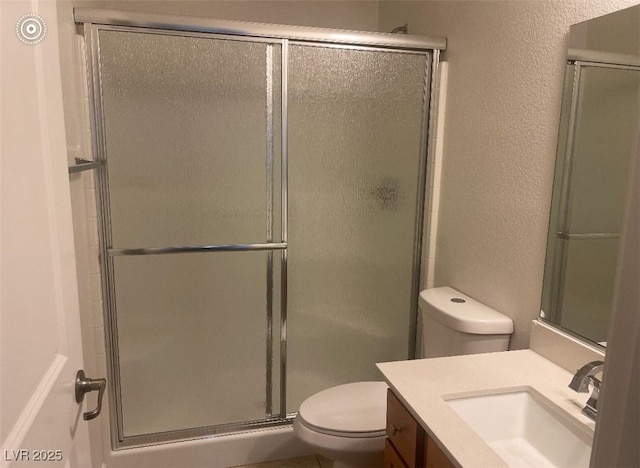 bathroom with vanity, a textured wall, a stall shower, and toilet