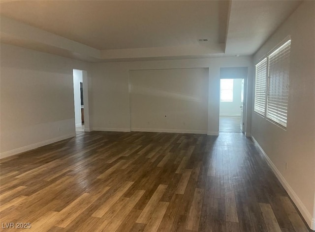 empty room with a raised ceiling, baseboards, visible vents, and dark wood-type flooring