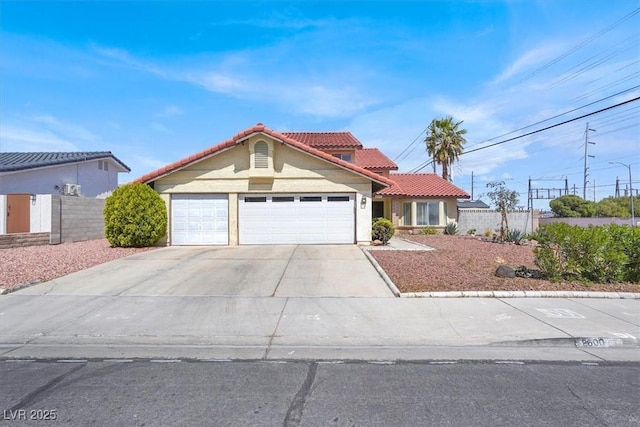 mediterranean / spanish-style home with a tile roof, concrete driveway, fence, and an attached garage
