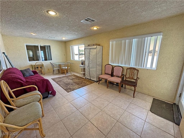 living room with a textured ceiling, a textured wall, visible vents, and light tile patterned floors