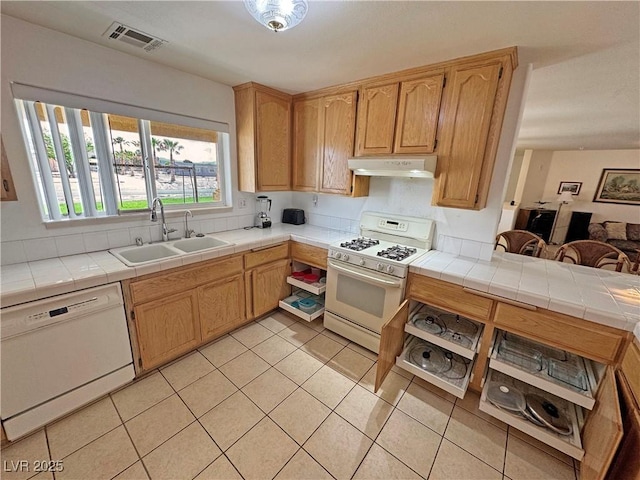 kitchen featuring white appliances, tile counters, under cabinet range hood, a sink, and light tile patterned floors