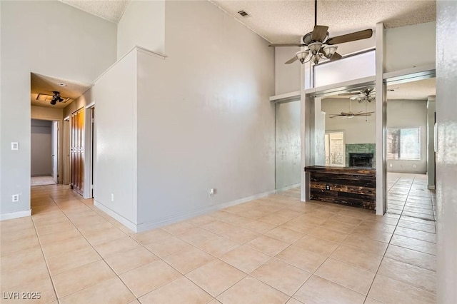 unfurnished living room with a textured ceiling, ceiling fan, light tile patterned flooring, and a high ceiling