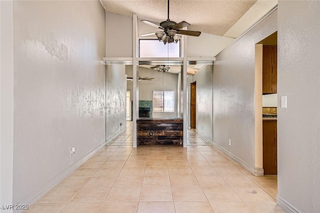 hall featuring light tile patterned floors, high vaulted ceiling, baseboards, and a textured ceiling