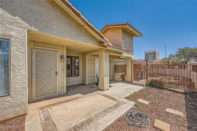 view of exterior entry with fence, a gate, and stucco siding