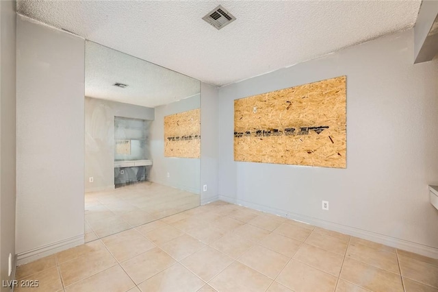 empty room featuring baseboards, tile patterned flooring, a textured ceiling, and visible vents