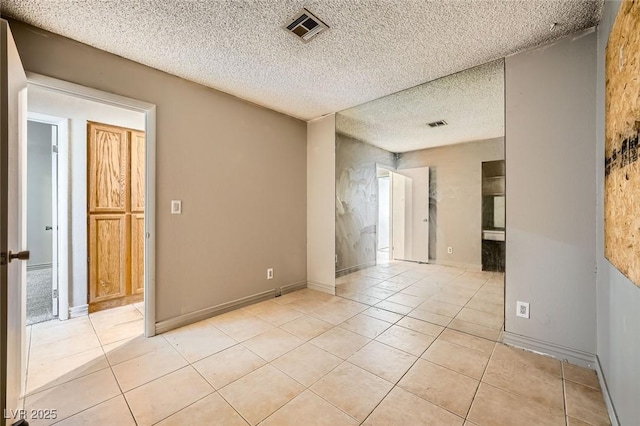 empty room with visible vents, a textured ceiling, baseboards, and light tile patterned flooring