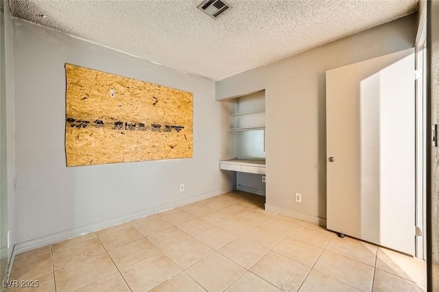 unfurnished bedroom featuring a textured ceiling, visible vents, built in study area, baseboards, and light tile patterned flooring