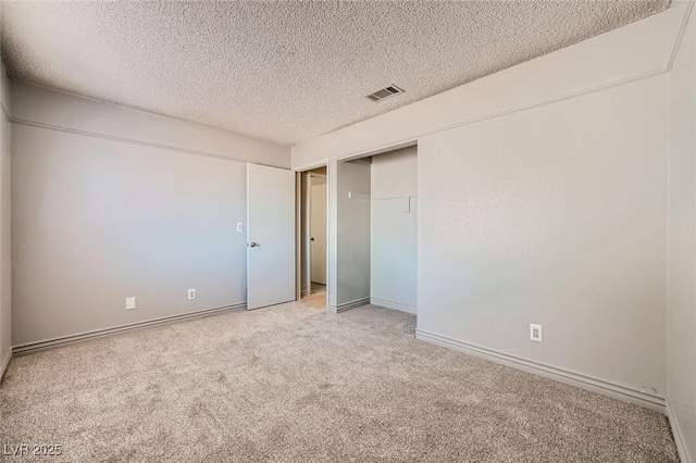 unfurnished bedroom featuring baseboards, light carpet, a textured ceiling, and visible vents