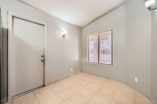 unfurnished room featuring baseboards, light tile patterned flooring, and vaulted ceiling