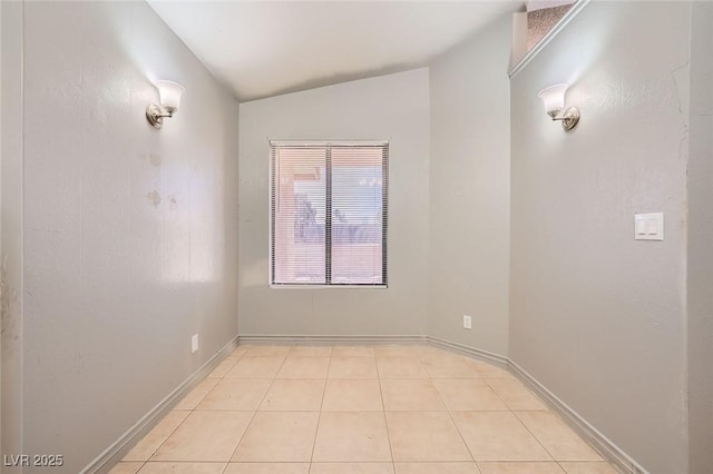 empty room with baseboards, light tile patterned flooring, and lofted ceiling