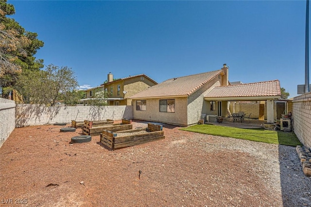 rear view of property featuring a tiled roof, a patio area, a vegetable garden, a fenced backyard, and stucco siding