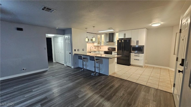 kitchen featuring wall chimney range hood, light wood-type flooring, a peninsula, appliances with stainless steel finishes, and visible vents