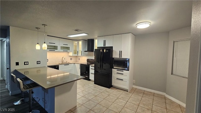 kitchen featuring black appliances, a breakfast bar, a peninsula, wall chimney exhaust hood, and visible vents