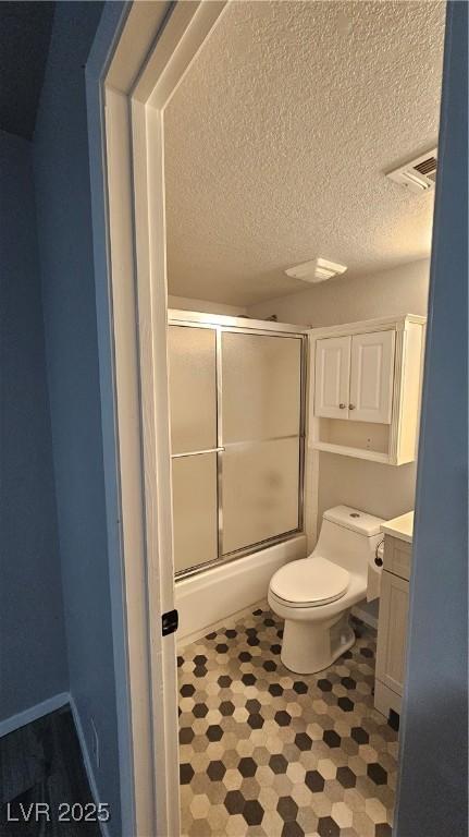 bathroom with visible vents, toilet, vanity, bath / shower combo with glass door, and a textured ceiling