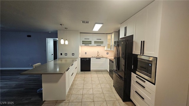 kitchen featuring visible vents, a sink, black appliances, a peninsula, and white cabinetry
