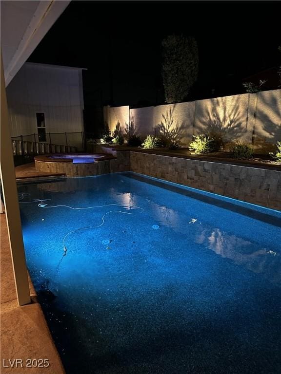pool at twilight featuring a fenced in pool and an in ground hot tub