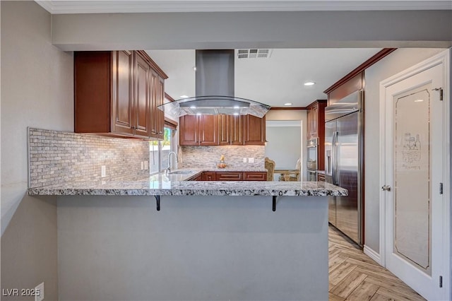 kitchen featuring light stone countertops, stainless steel appliances, a peninsula, range hood, and visible vents