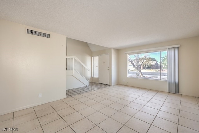 unfurnished room with visible vents, a textured ceiling, stairway, and light tile patterned flooring