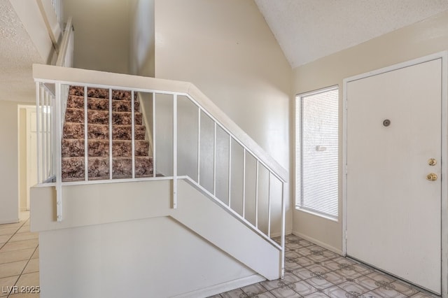 tiled entrance foyer with stairway, vaulted ceiling, and a textured ceiling