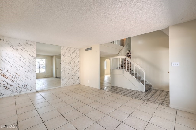 tiled empty room featuring an accent wall, stairs, wallpapered walls, a textured ceiling, and visible vents