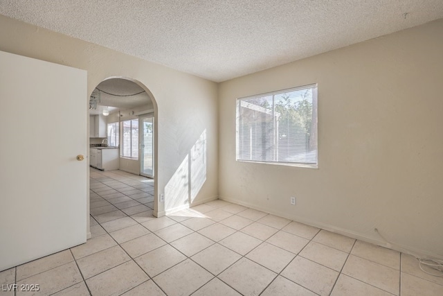 spare room featuring arched walkways, a textured ceiling, and light tile patterned floors