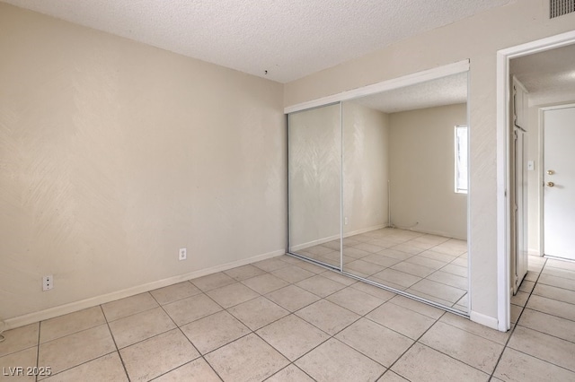 unfurnished bedroom with a textured ceiling, a closet, light tile patterned flooring, baseboards, and visible vents