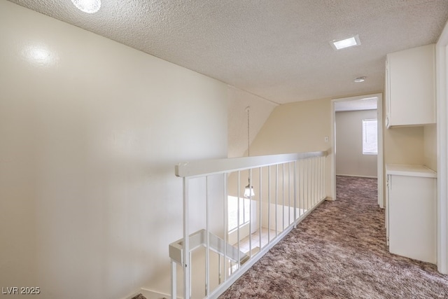 hall featuring an upstairs landing, carpet, and a textured ceiling