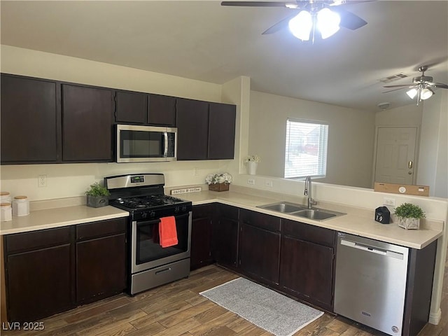 kitchen with wood finished floors, a sink, ceiling fan, stainless steel appliances, and a peninsula
