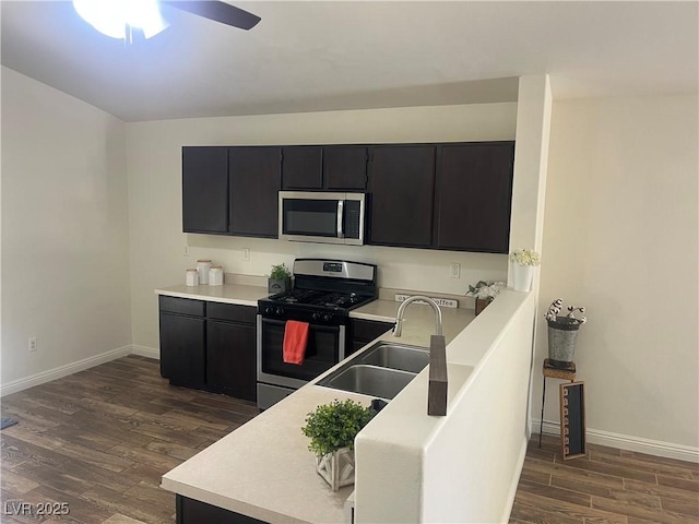 kitchen featuring stainless steel appliances, dark cabinetry, a sink, baseboards, and dark wood-style flooring