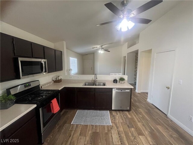kitchen with vaulted ceiling, a sink, stainless steel appliances, light countertops, and dark wood-style flooring