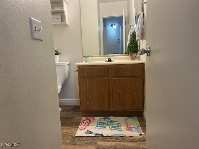 half bath with toilet, wood finished floors, vanity, a textured wall, and baseboards