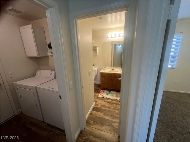laundry area featuring dark wood finished floors, visible vents, a sink, washing machine and dryer, and cabinet space