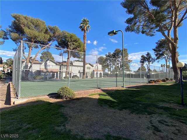 view of tennis court with a yard and fence